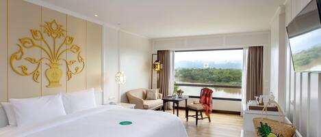 A hotel room with a large bed, a desk, a chair, and a view of a river.