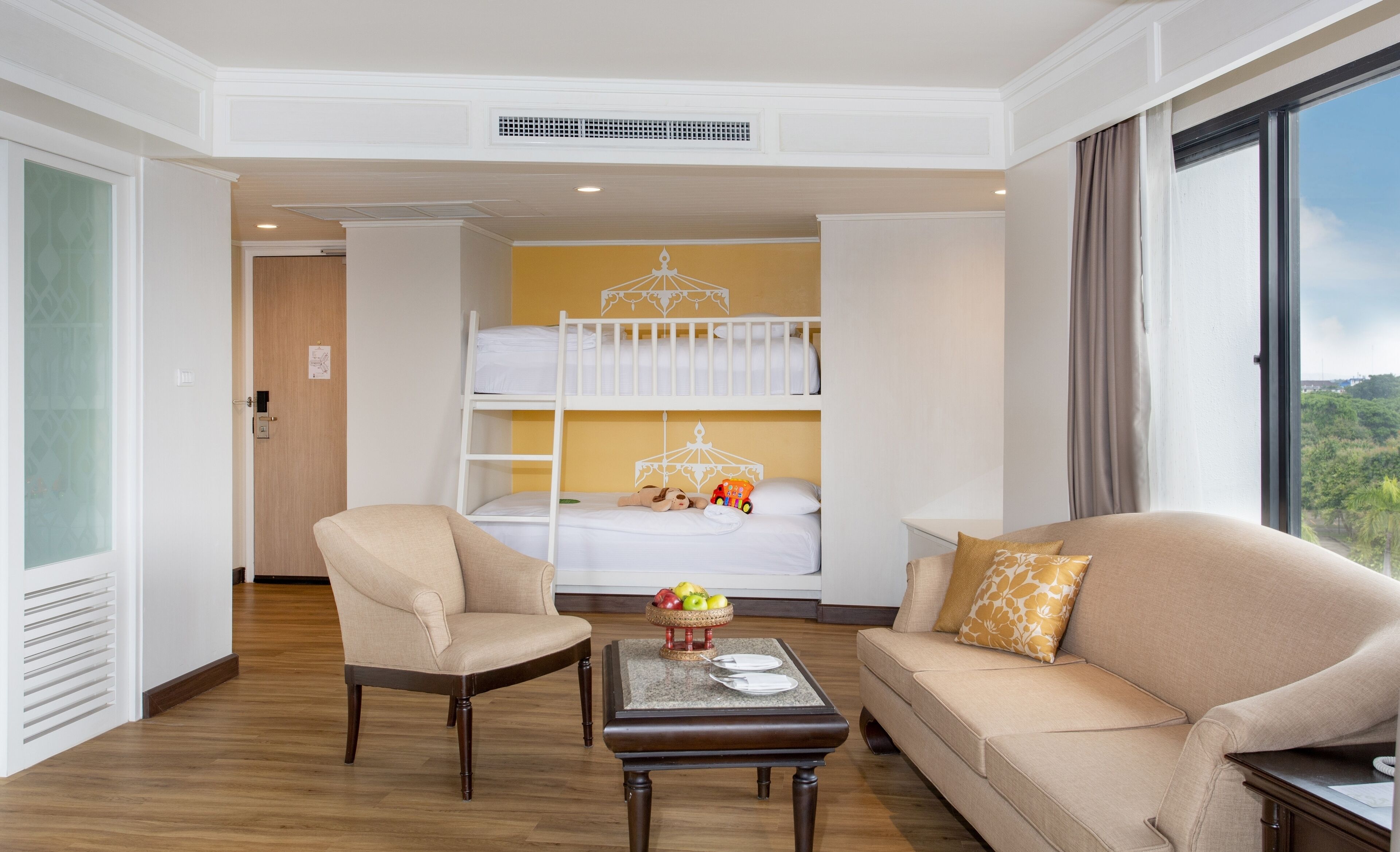 Quarto de hotel com uma cama de solteiro, um sofá, uma cadeira e uma pequena mesa com uma fruteira.