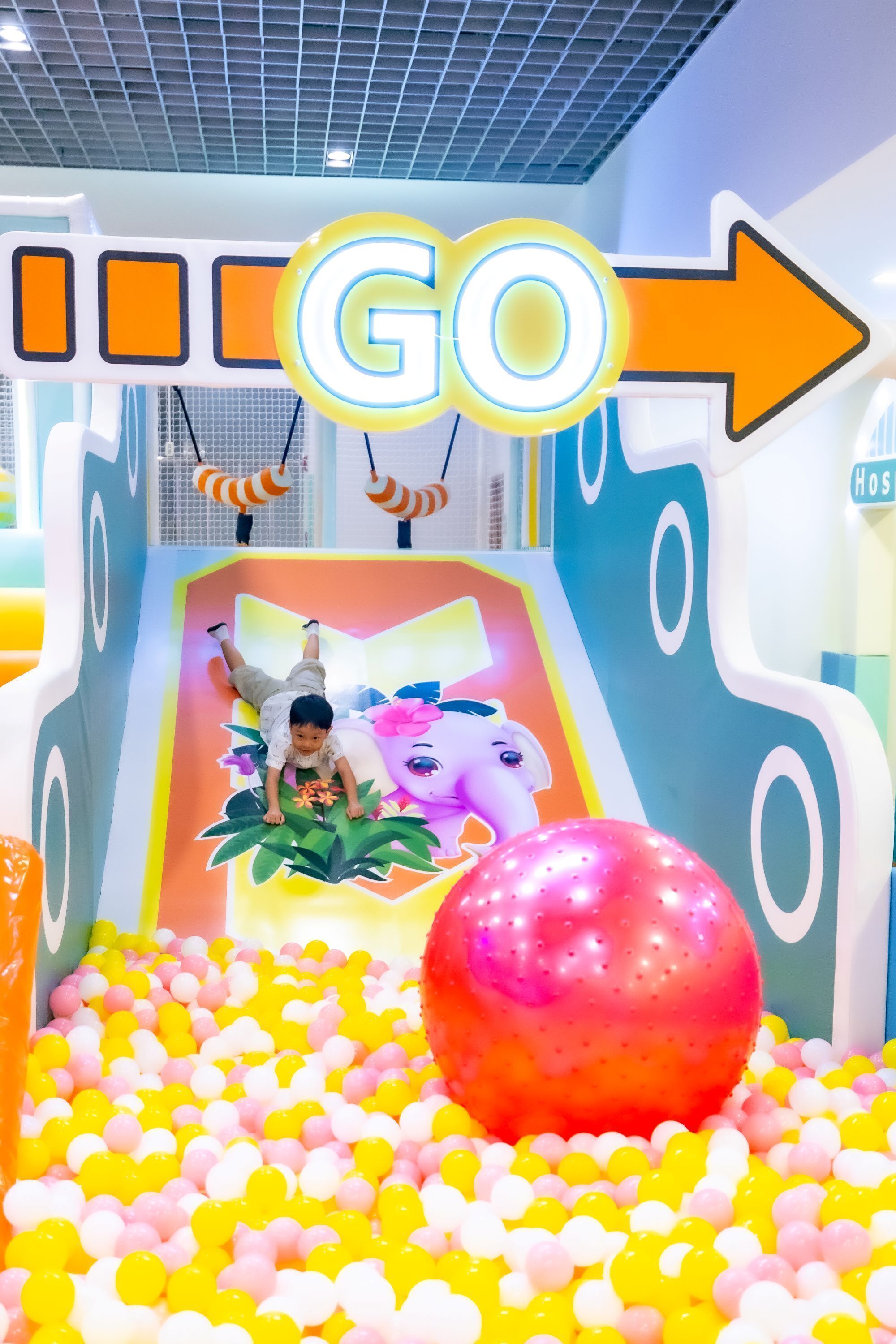 Niño jugando en un área de juegos interior colorida con un tobogán, piscina de pelotas y un cartel que dice 'GO'.