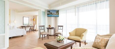 A hotel room with a bed, a sitting area with a sofa and armchairs, a coffee table, a desk with a chair, and a TV on the wall.