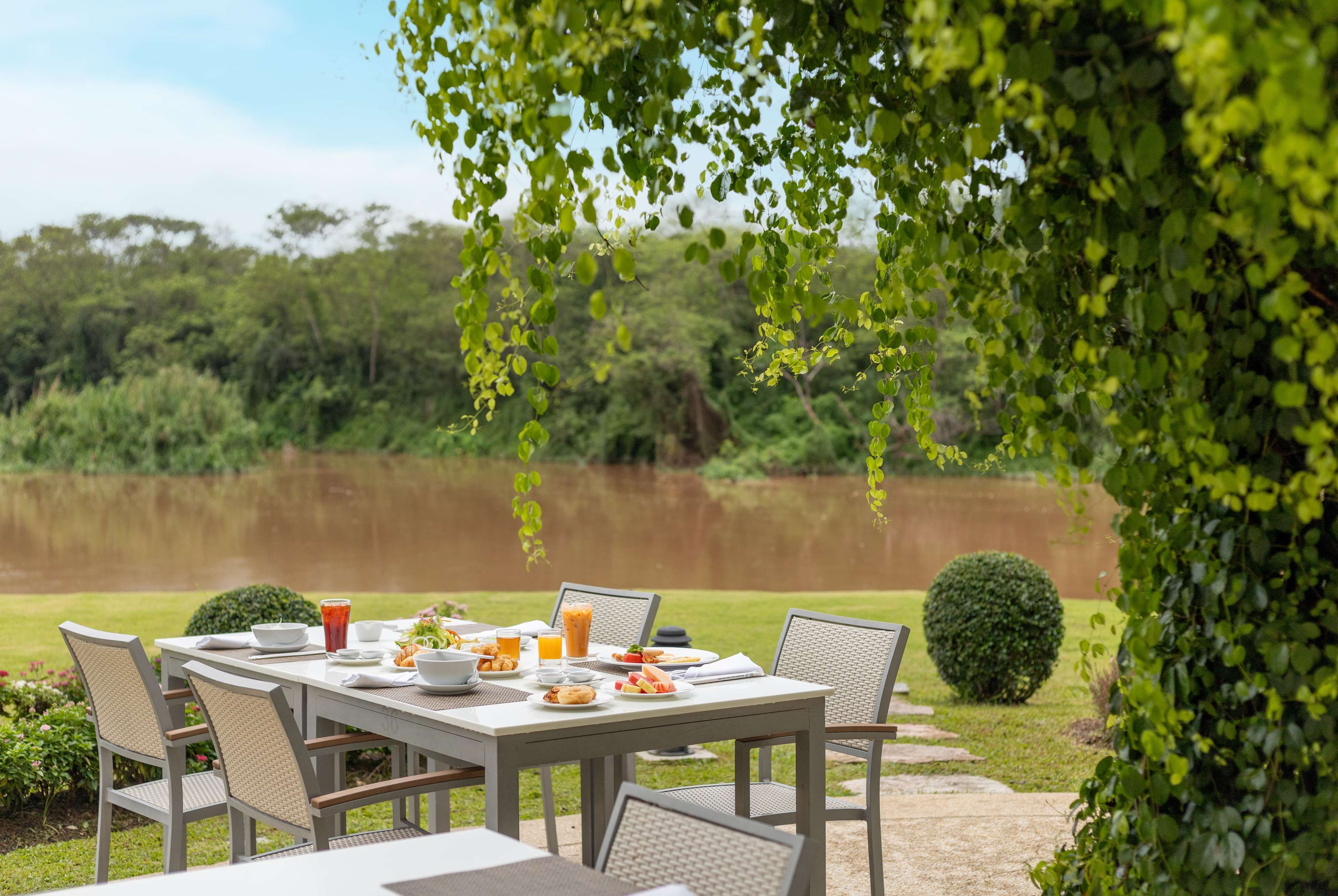 An outdoor dining area with a table set for breakfast, surrounded by chairs, and overlooking a body of water.
