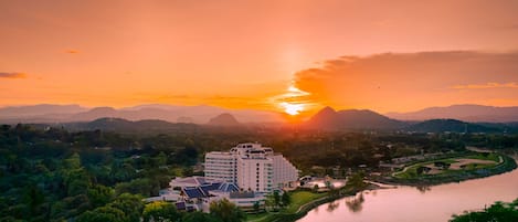 A modern hotel with multiple floors, surrounded by lush greenery and a river.