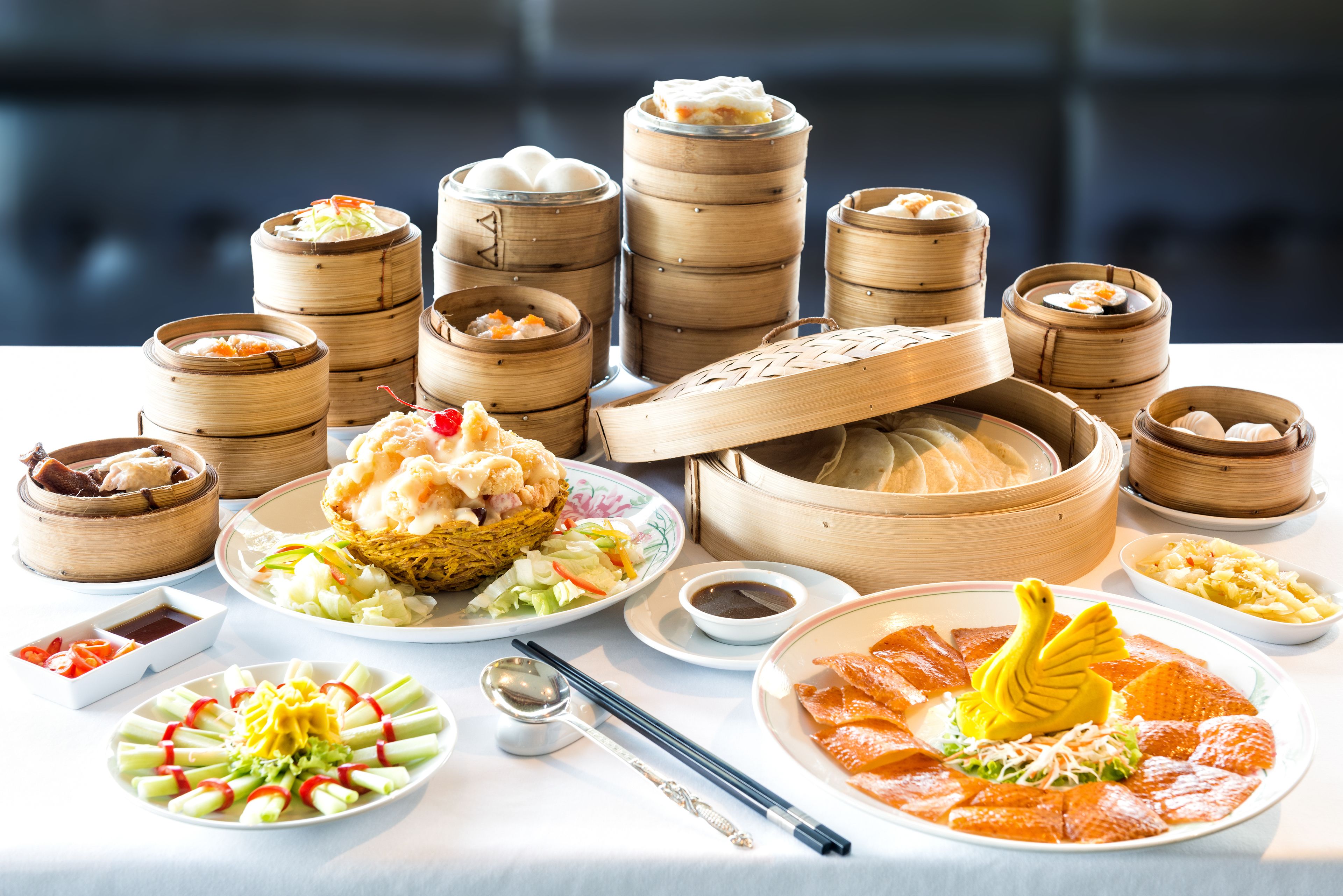 A table with various dishes, including dim sum, a plate with a swan-shaped decoration, and a bowl of soup.