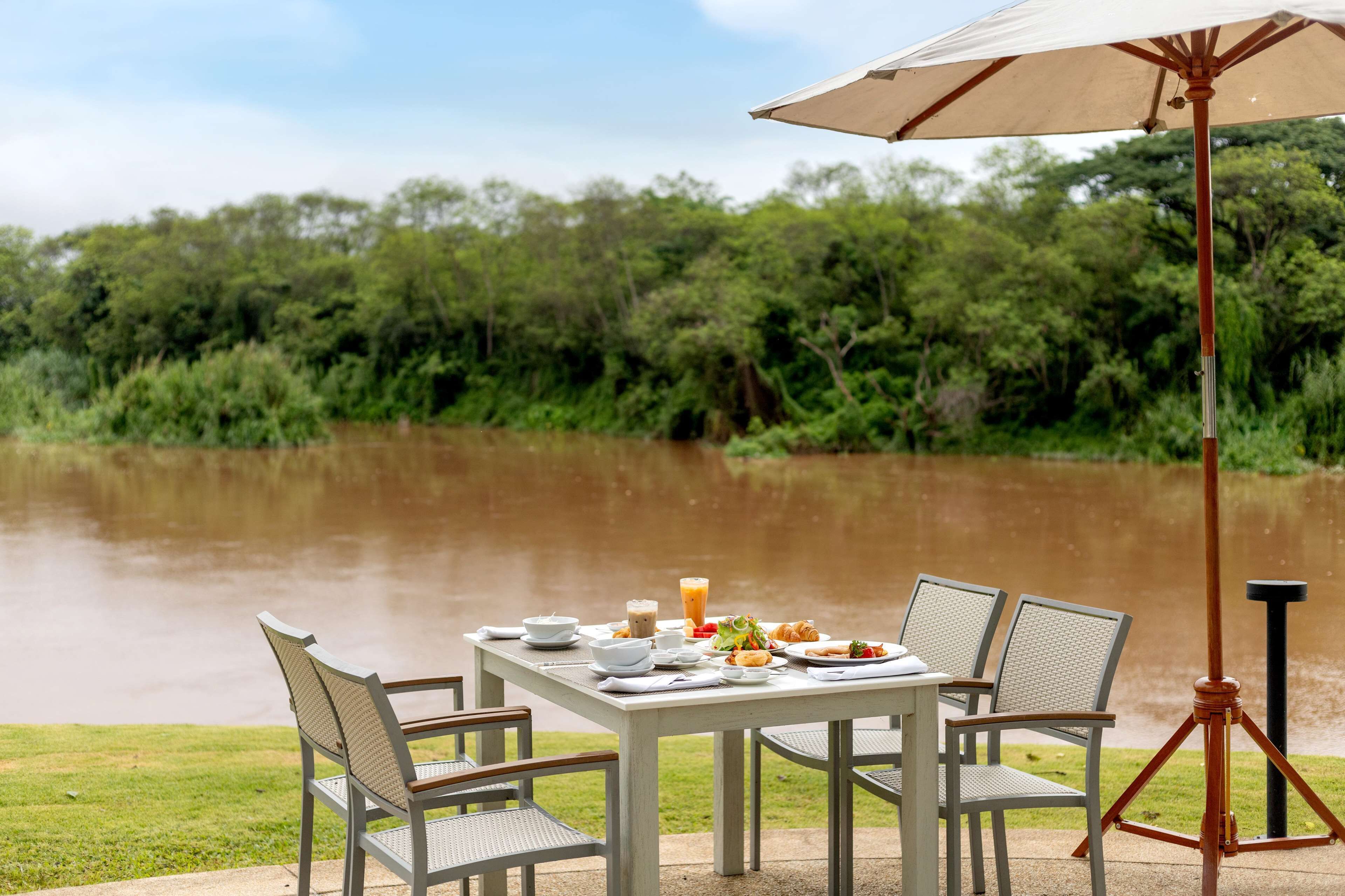 A dining table set outdoors with chairs, a table umbrella, and a tripod stand.