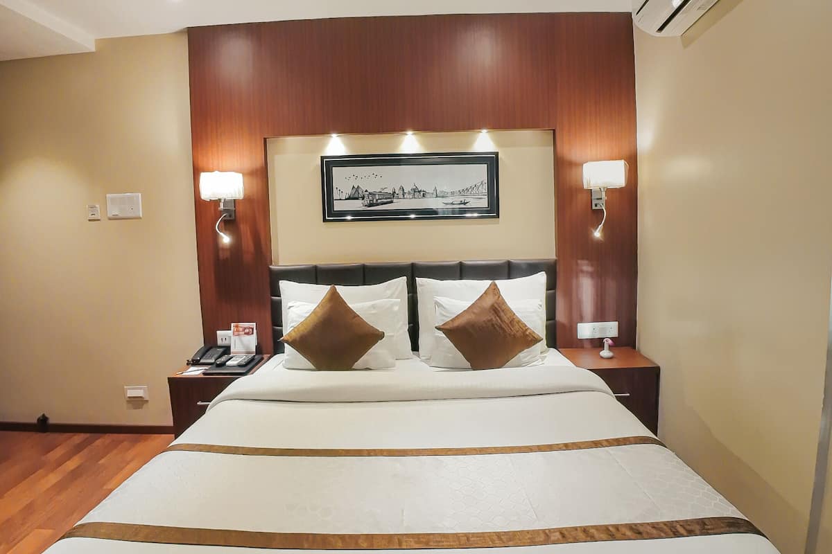 Une chambre d’hôtel avec un grand lit, une tête de lit en bois, deux tables de chevet avec des lampes, un appareil de climatisation et un tableau encadré au mur.