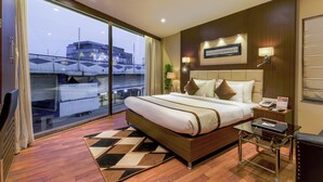 A hotel room with a large bed, a glass table, a nightstand, and a view of the cityscape. - Hotel Sawood International (Kolkata)