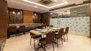 A dining area with a long table, multiple chairs, and a booth. - Hotel Sawood International (Kolkata)