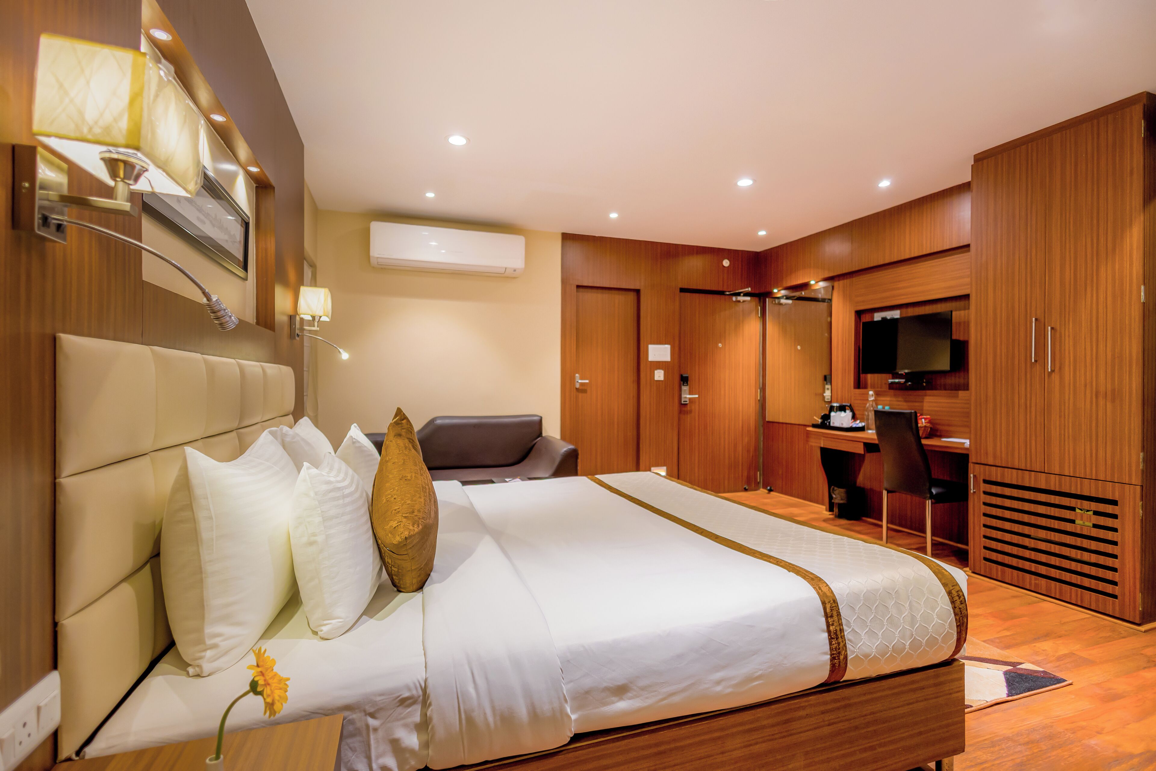 A hotel room with a bed, a desk, a chair, a television, and an air conditioning unit.