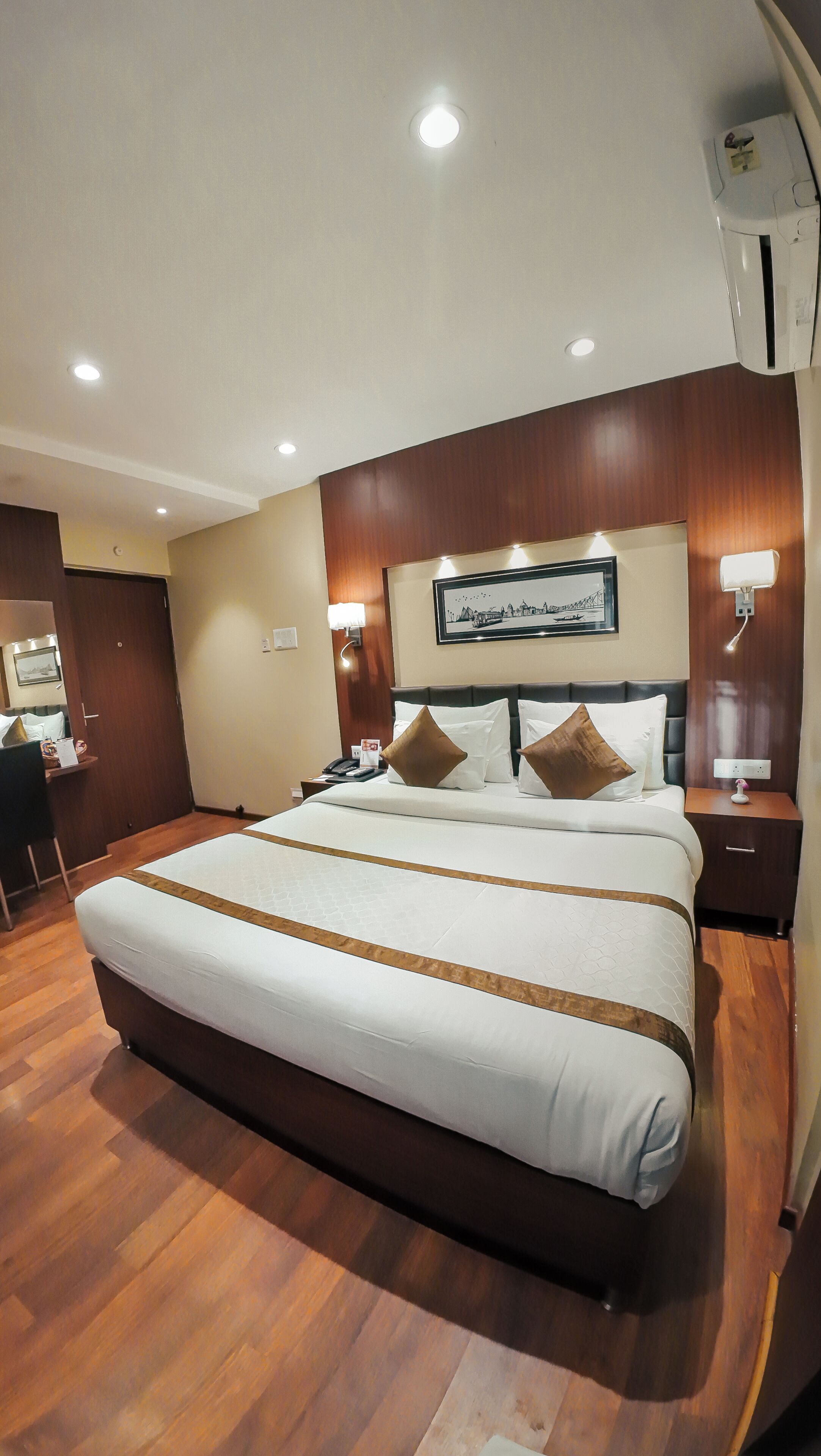 Een hotelkamer met een groot bed, houten vloer, een bureau en een ingelijst schilderij aan de muur.