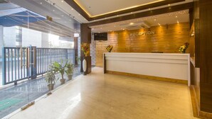 A reception area with a wooden reception desk, potted plants, and a chandelier. - Hotel Sawood International (Kolkata)