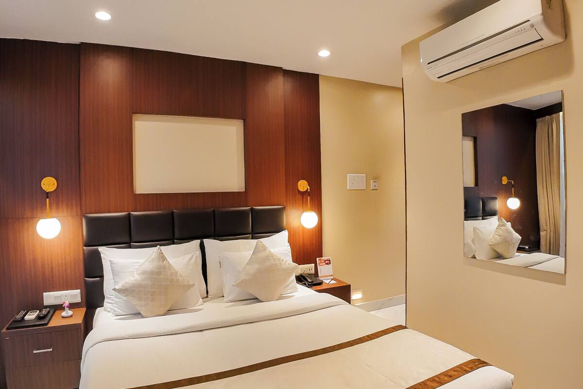 Une chambre d’hôtel avec un grand lit, des boiseries, un climatiseur fixé au mur et un miroir qui reflète une partie de la pièce.