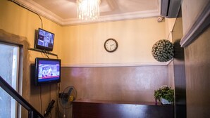 A room with a wooden bench, a clock, a television mounted on the wall, and a ceiling fan. - Ikeja Transit Hotel (Lagos)