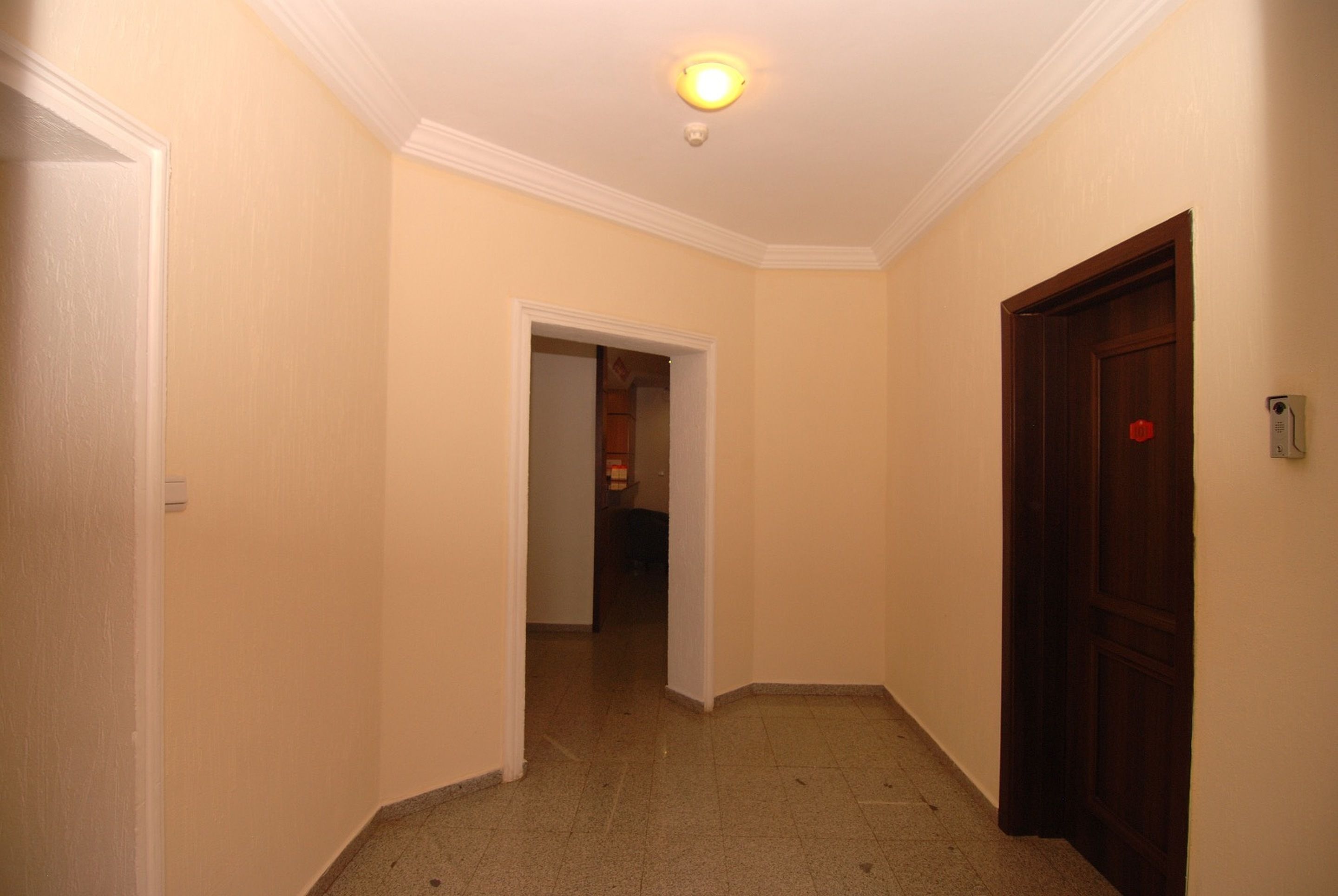 A narrow hallway with beige walls, a wooden door on the right, and a white door on the left.