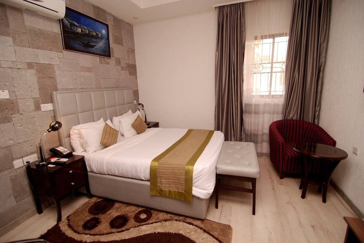 Ein Hotelzimmer mit Bett, Nachttisch, Lampe und einem Sessel.