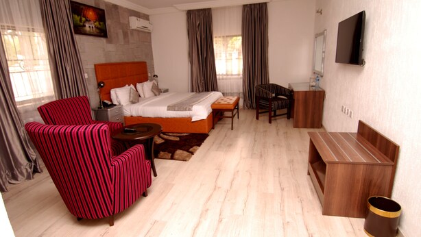 Een hotelkamer met een bed, een rood gestreepte fauteuil, een houten bankje, een kleine tafel en een aan de muur bevestigde televisie.