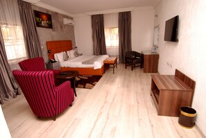 Una camera d'albergo con un letto, una poltrona a righe rosse, una panca di legno, un tavolino e una TV fissata al muro.