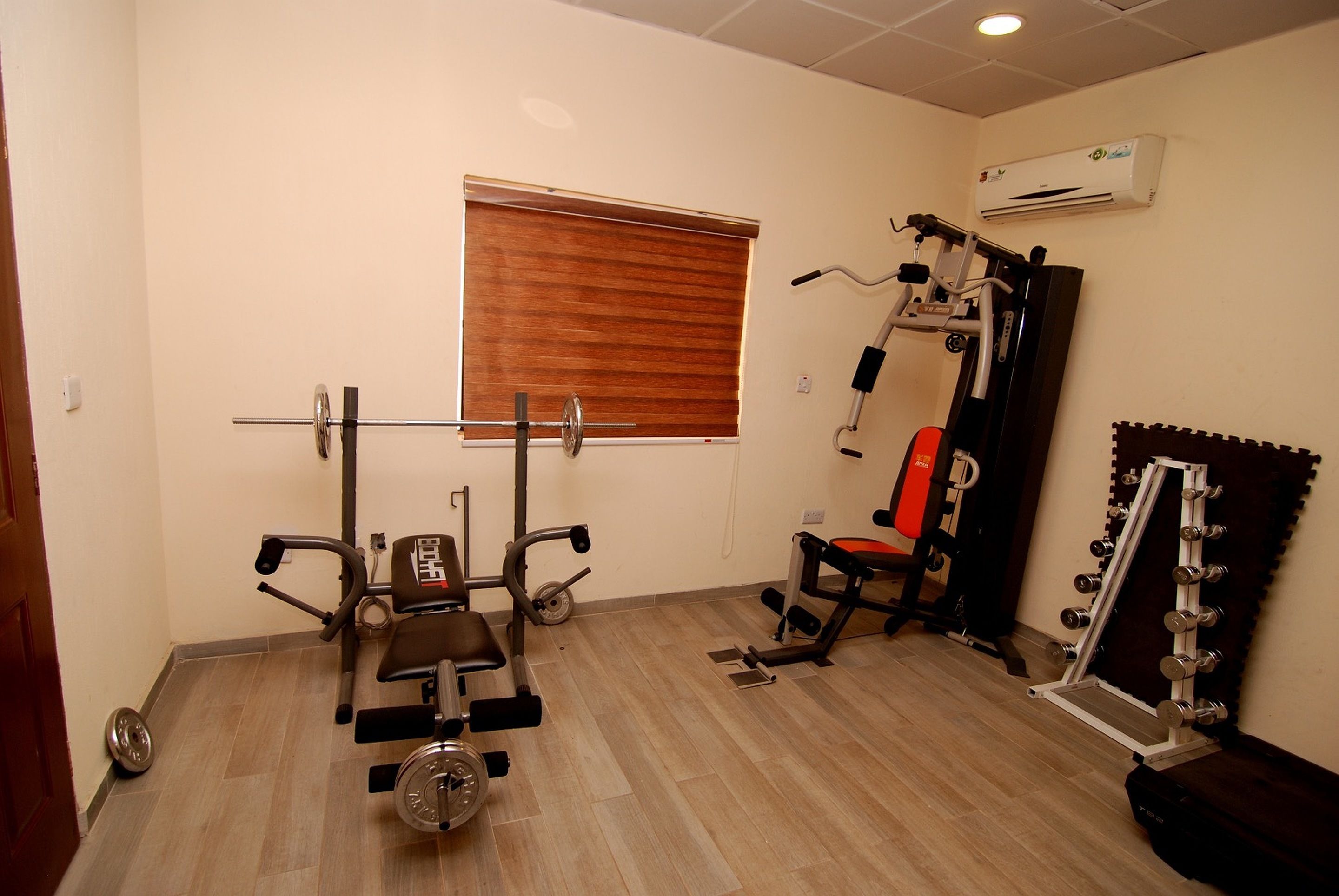 A gym with a weight bench, a bench press, a squat rack, and a bench press with dumbbells.