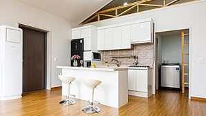A modern kitchen with white cabinets, a central island, and two bar stools. - Jeju Platinum Caravan (Jeju City)