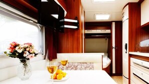 A compact RV interior with a dining area, a kitchenette, and a small sleeping space. - Jeju Platinum Caravan (Jeju City)