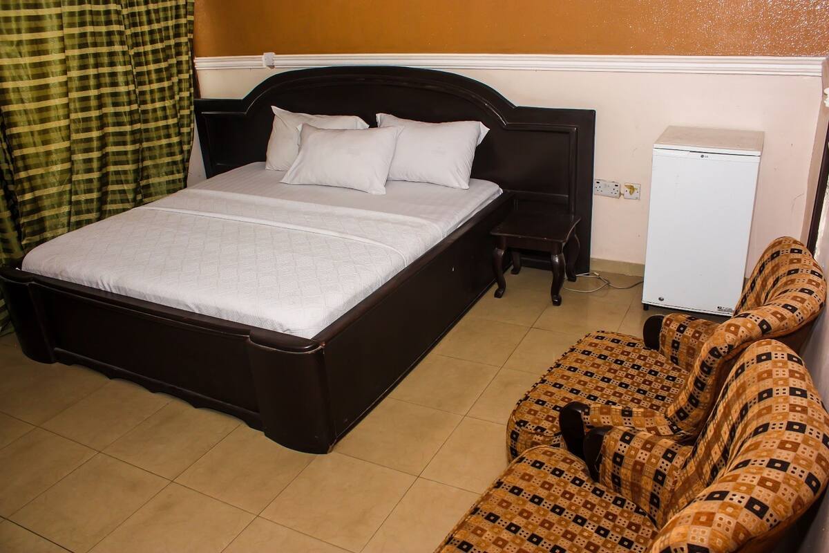 A hotel room with a large bed, a bedside table, a small desk, and a refrigerator.
