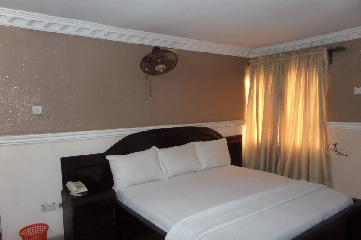 A neatly made bed with white linens, a dark headboard, and a bedside table with a telephone.