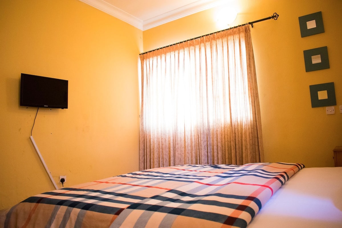 A room with a bed, a television mounted on the wall, and a window with curtains.