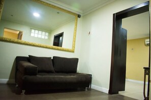 A room with a dark brown sofa, a large mirror with a gold frame, and a wooden door. - Sugarland Apartments VI (Lagos)
