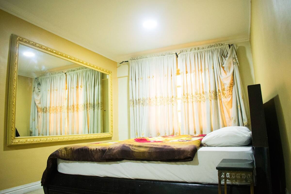A hotel room with a bed, a large mirror, and curtains.