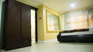 A bedroom with a large wardrobe, a bed with a brown blanket, a large mirror, and a window with curtains.