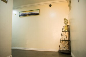A hallway with a framed landscape painting on the wall, a decorative metal stand with a horse figure, and a white baseboard. - Sugarland Apartments VI (Lagos)