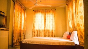 A room with a bed, curtains, a ceiling fan, and a small table. - Amenze Guest House (Lagos)