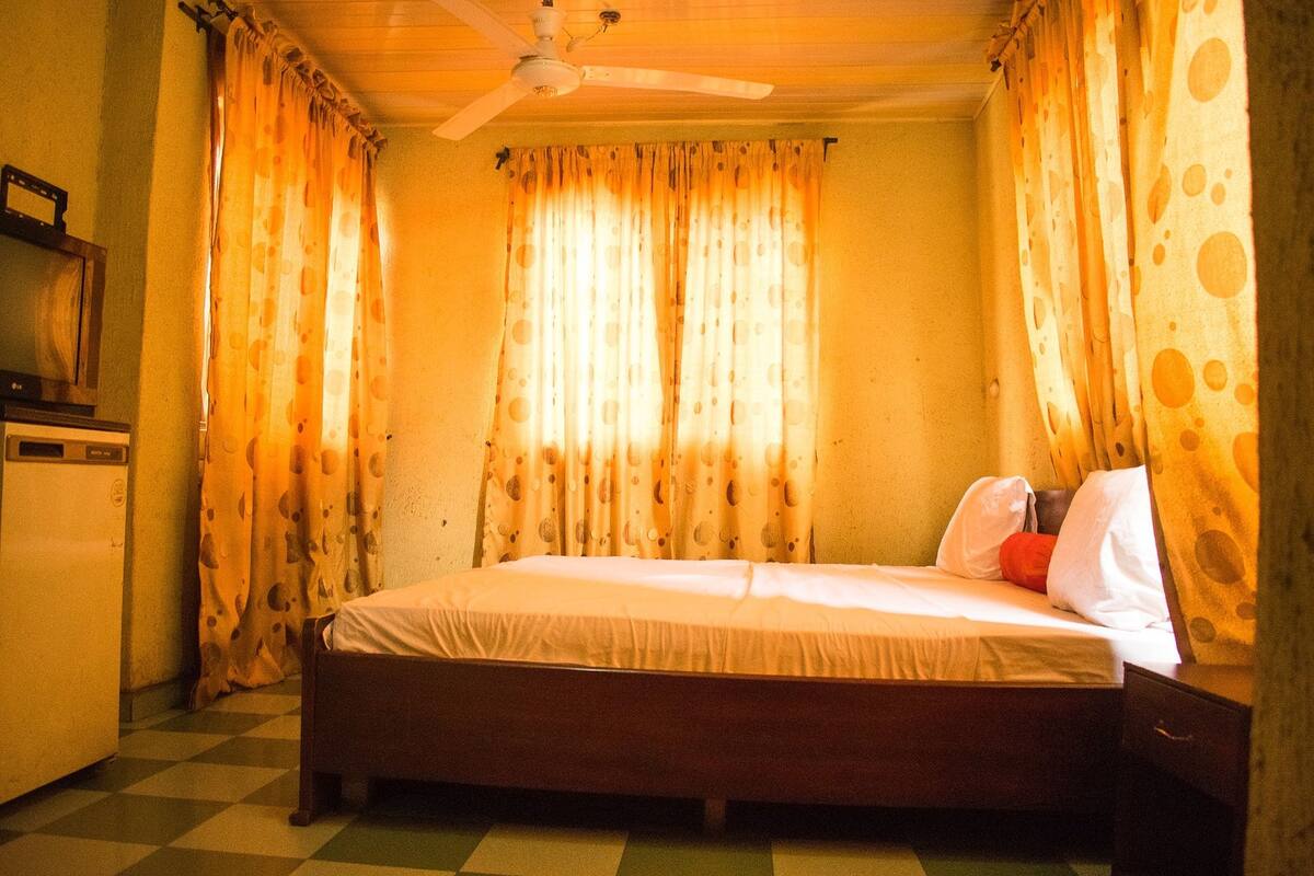 A room with a bed, curtains, a ceiling fan, and a small table.