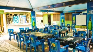 A restaurant with outdoor seating, tables with blue chairs, and walls decorated with Harp beer advertisements. - Amenze Guest House (Lagos)