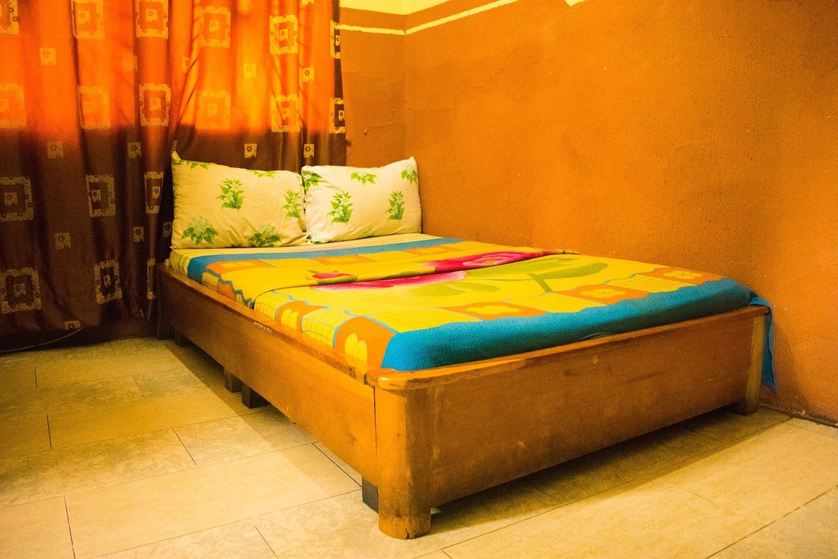 A bed with a colorful bedspread, a wooden headboard, and a curtain with a geometric pattern.