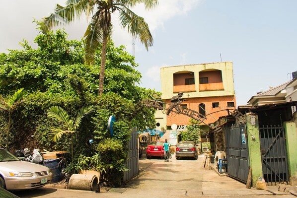A narrow street with parked cars and a building with a balcony in the background.