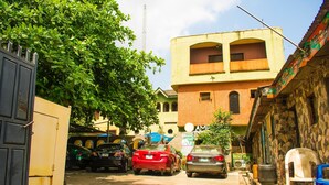 A narrow street with parked cars, a building with a hipped roof, and a tree. - Amenze Guest House (Lagos)