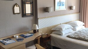 Een hotelkamer met een bed, een bureau met stoel, een lamp en verschillende spiegels aan de muur.