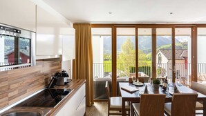 Una cocina moderna con un amplio ventanal, un comedor con una mesa dispuesta para dos personas y vistas a un paisaje montañoso.