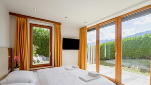 Un dormitorio con una cama grande, dos ventanas con cortinas, un televisor de pantalla plana y vistas a un paisaje montañoso.