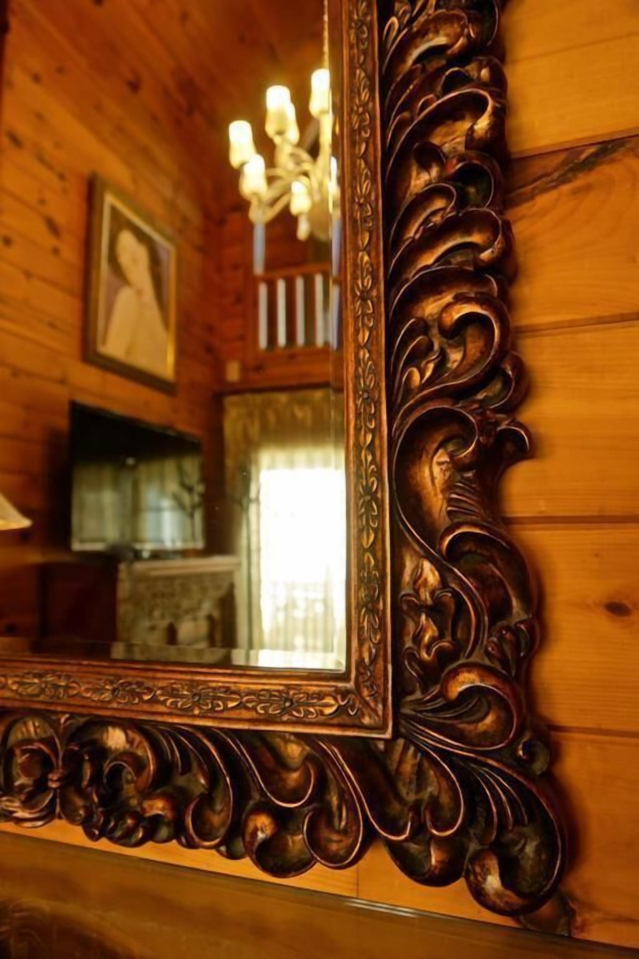A wooden interior with a large ornate mirror reflecting a chandelier and a framed picture.