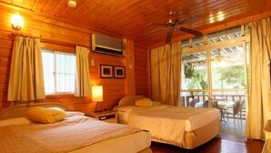 Una habitación tipo cabaña de madera con dos camas, un ventilador de techo y un balcón con mobiliario exterior.