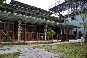 A building with a covered porch, a fenced area, and two sheep on the grass. - Sun Moon Lake Full House Resort (Yuchi)