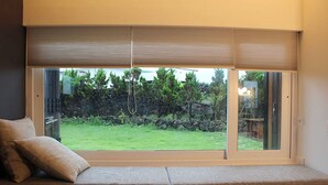 A room with a large window, a cushioned bench, and a stone wall outside. - Void (Jeju City)