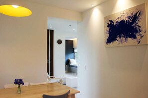 Un espace repas moderne avec une table en bois, des chaises et un vase de fleurs. Un tableau orne le mur, et une horloge y est également accrochée.