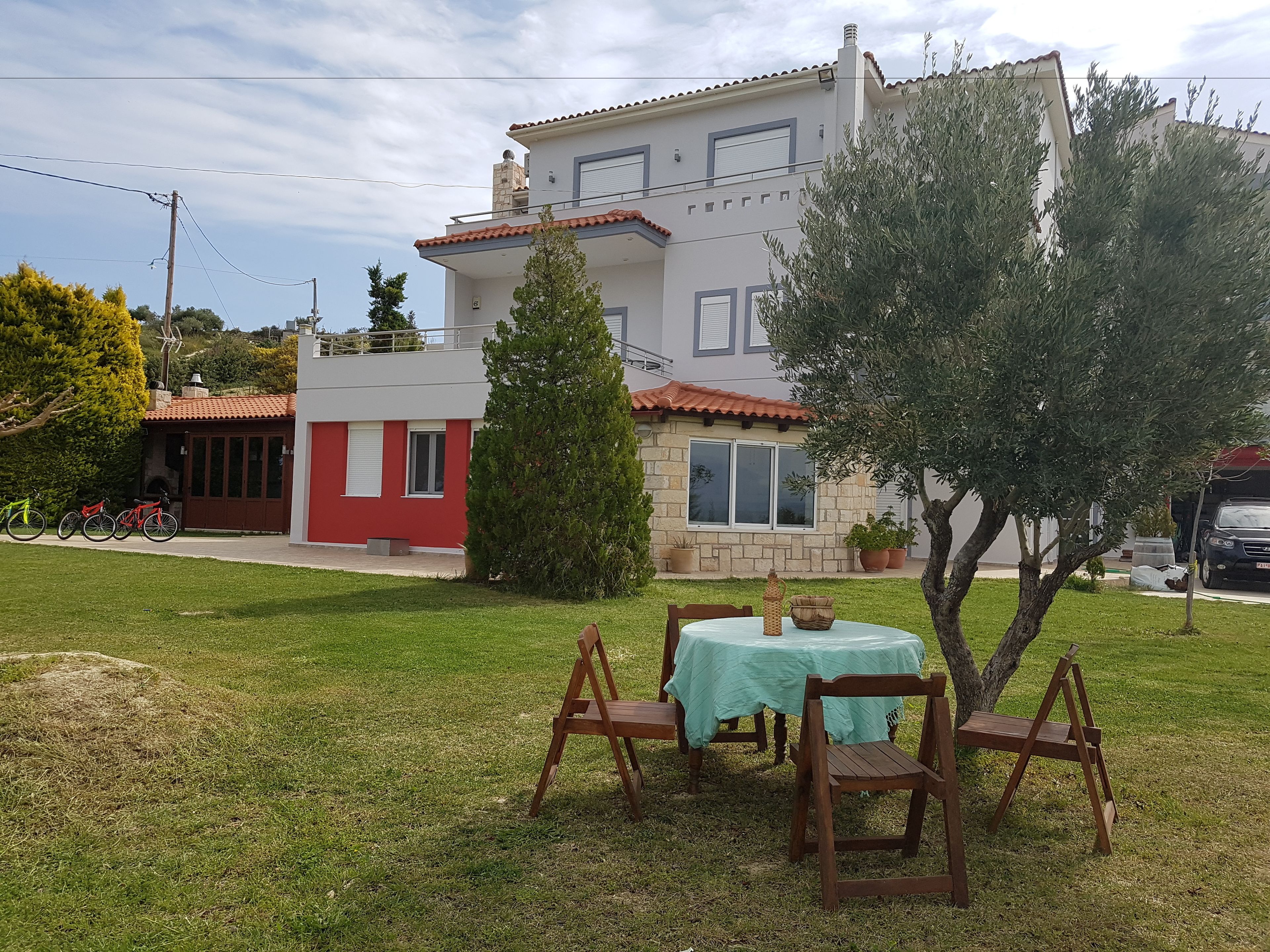 A patio with a table and chairs, a small red building, and a larger house with a tiled roof in the background.