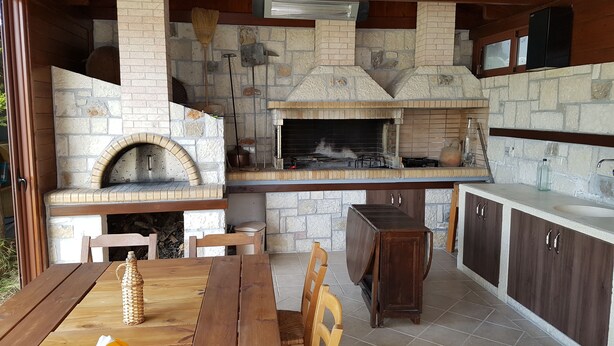 Una cocina rústica al aire libre con horno de piedra, mesa de madera y taburetes de bar.