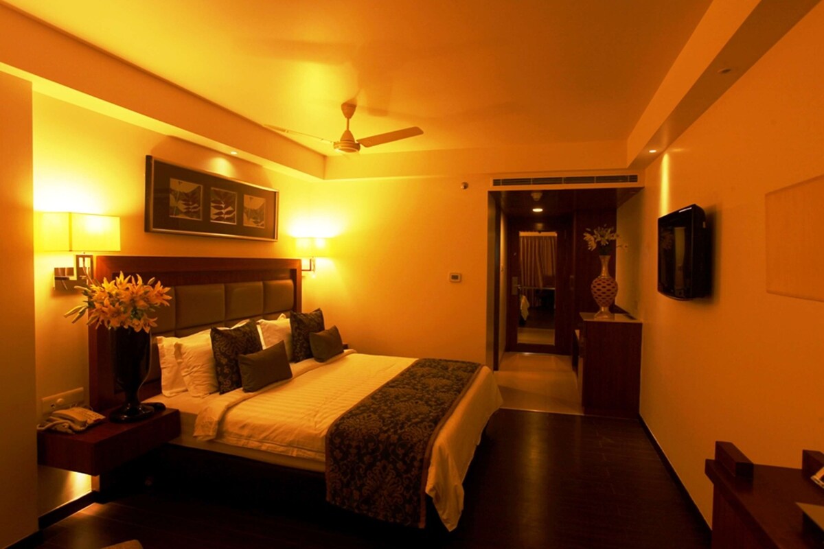 A hotel room with a bed, bedside lamps, a ceiling fan, a nightstand, and a TV on the wall.