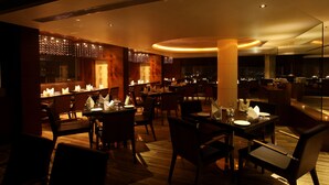 Un restaurante tenuemente iluminado con mesas y sillas de madera, iluminación cálida y un diseño interior moderno.