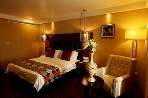 A hotel room with a large bed, a chair, a vase with flowers, and a painting on the wall.