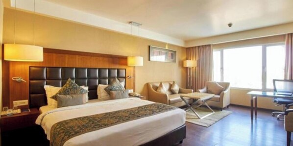 A hotel room with a large bed, a sofa, a desk, and a TV.
